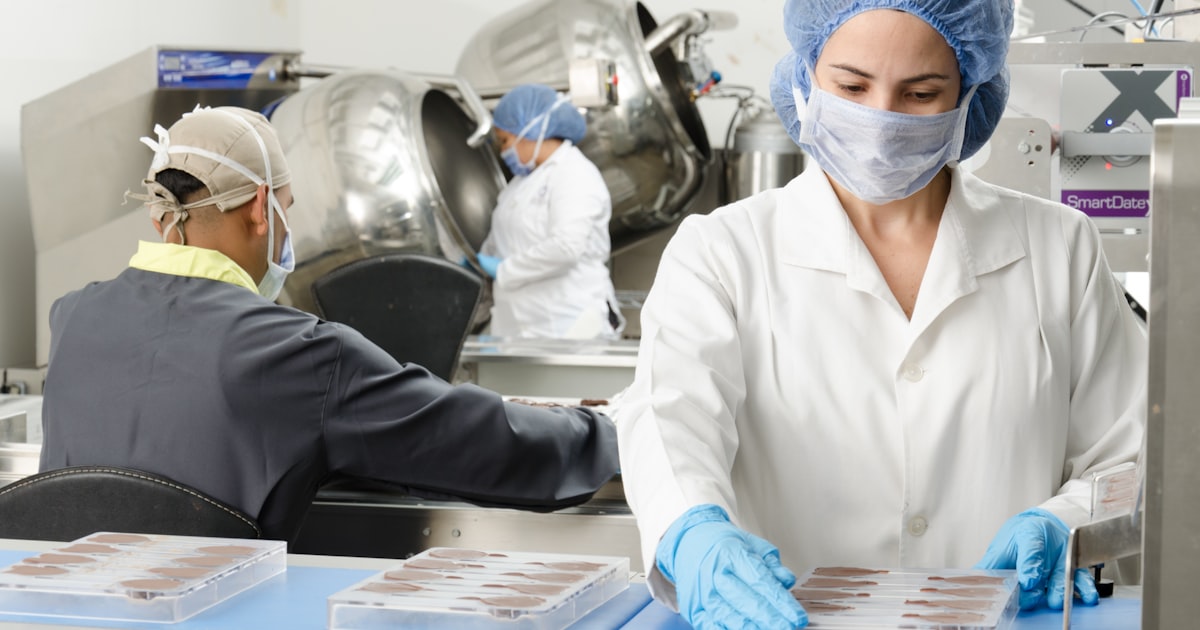 Food production staff in protective coats, hairnets and gloves on a packing line