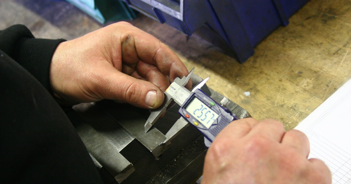 Technician measuring a machined metal part with a digital caliper
